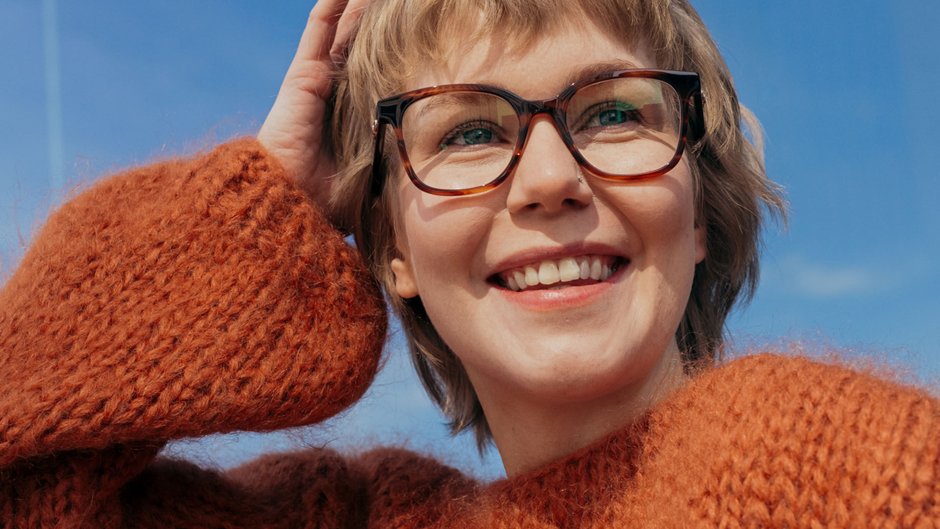 Nuori nainen ulkona, yll&auml;&auml;n oranssi neule ja ruskeat silm&auml;lasit